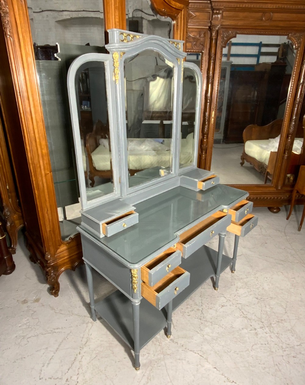 A plummet grey painted French dressing table featuring a central tri-fold mirror, brass embellishments, a glass top, multiple drawers, and turned legs. View III