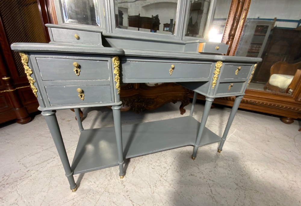 A plummet grey painted French dressing table featuring a central tri-fold mirror, brass embellishments, a glass top, multiple drawers, and turned legs. View VIII