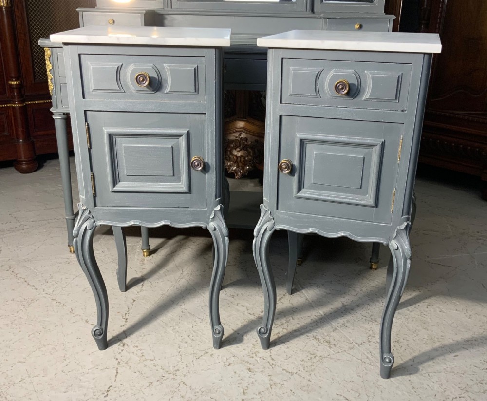A pair of plum grey painted French bedside cabinets with white marble tops, single drawers, cupboards, and carved cabriole legs.