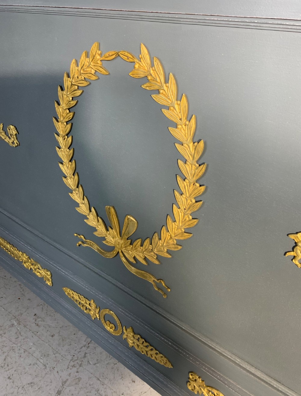 A grey painted French double bed frame decorated with gold brass mounts, featuring a central laurel wreath motif and a pediment headboard. View II