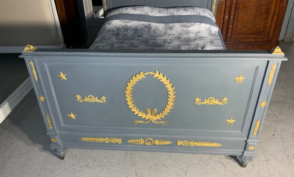 A grey painted French double bed frame decorated with gold brass mounts, featuring a central laurel wreath motif and a pediment headboard. View VI