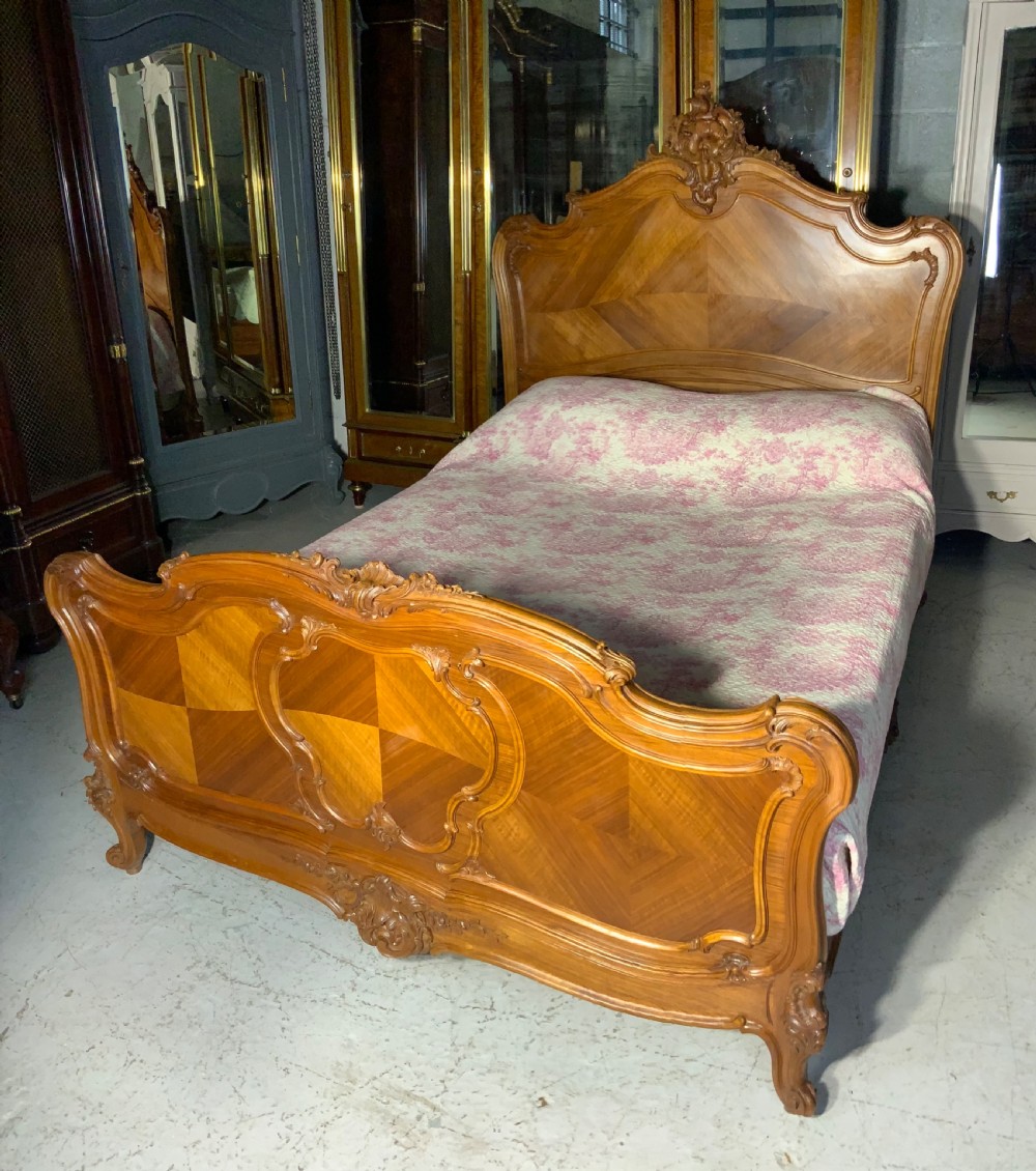A king size French Louis XV style wooden bed frame featuring a carved crest, parquetry panelwork, and curved legs.