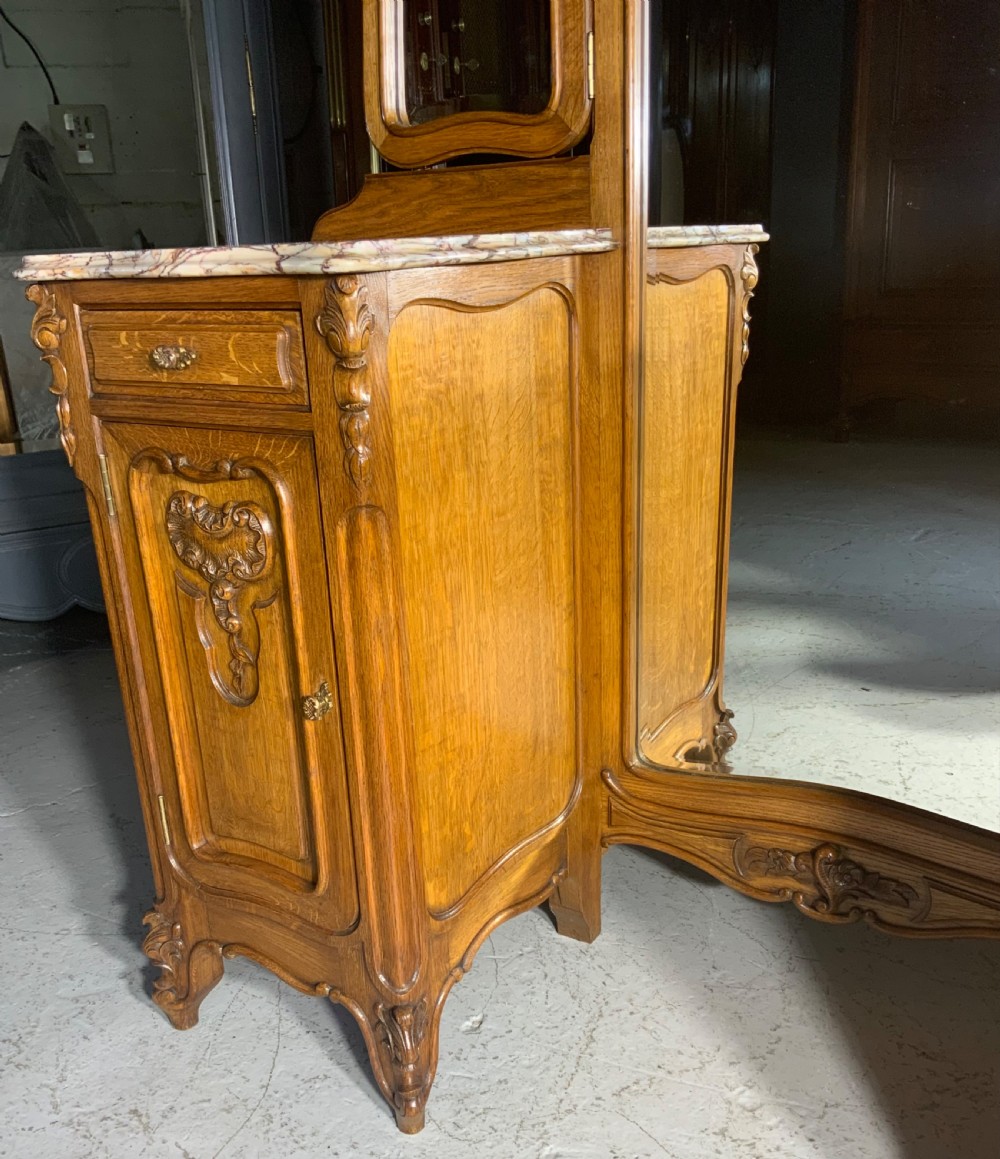 An antique carved oak French dressing table featuring twin marble-topped pedestals, carved foliate doors, and three framed glass mirrors. View IV
