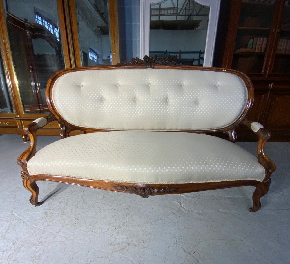 A French Rococo Revival rosewood canape featuring cream button-backed upholstery, carved cabriole legs, and a floral-carved top rail. View VI