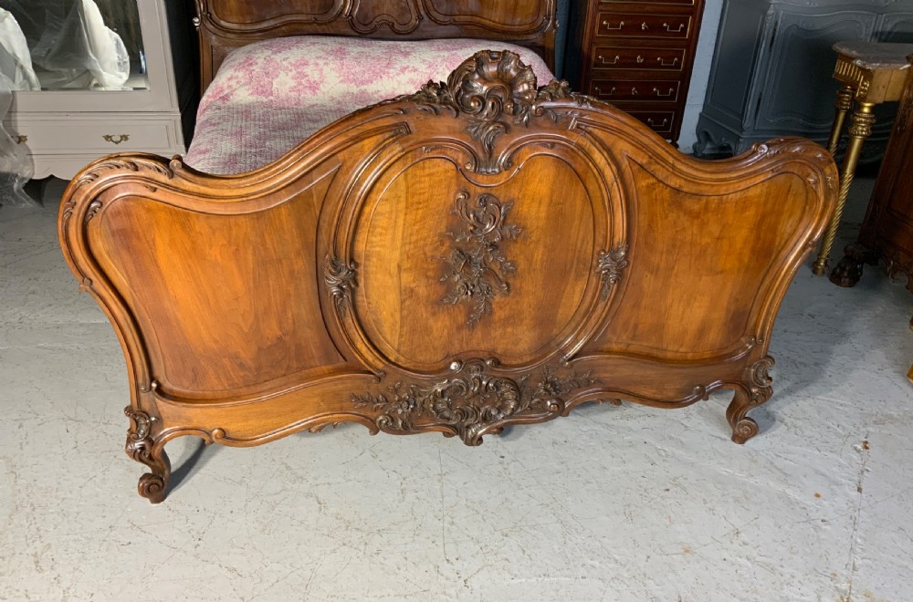 A carved French walnut bed frame with a high headboard and footboard featuring serpentine crests and detailed floral carvings. View VIII