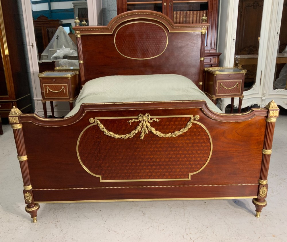 French Neoclassical mahogany bed frame featuring an oval marquetry panel, polished brass mounts, fluted columns, and two matching marble-topped bedside cabinets. View II