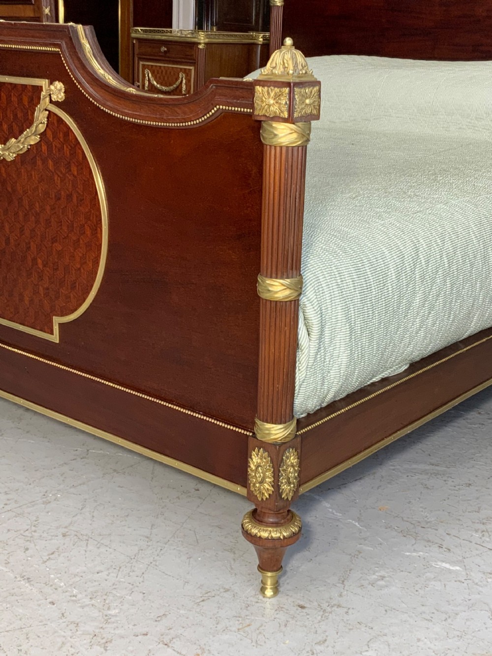French Neoclassical mahogany bed frame featuring an oval marquetry panel, polished brass mounts, fluted columns, and two matching marble-topped bedside cabinets. View IV