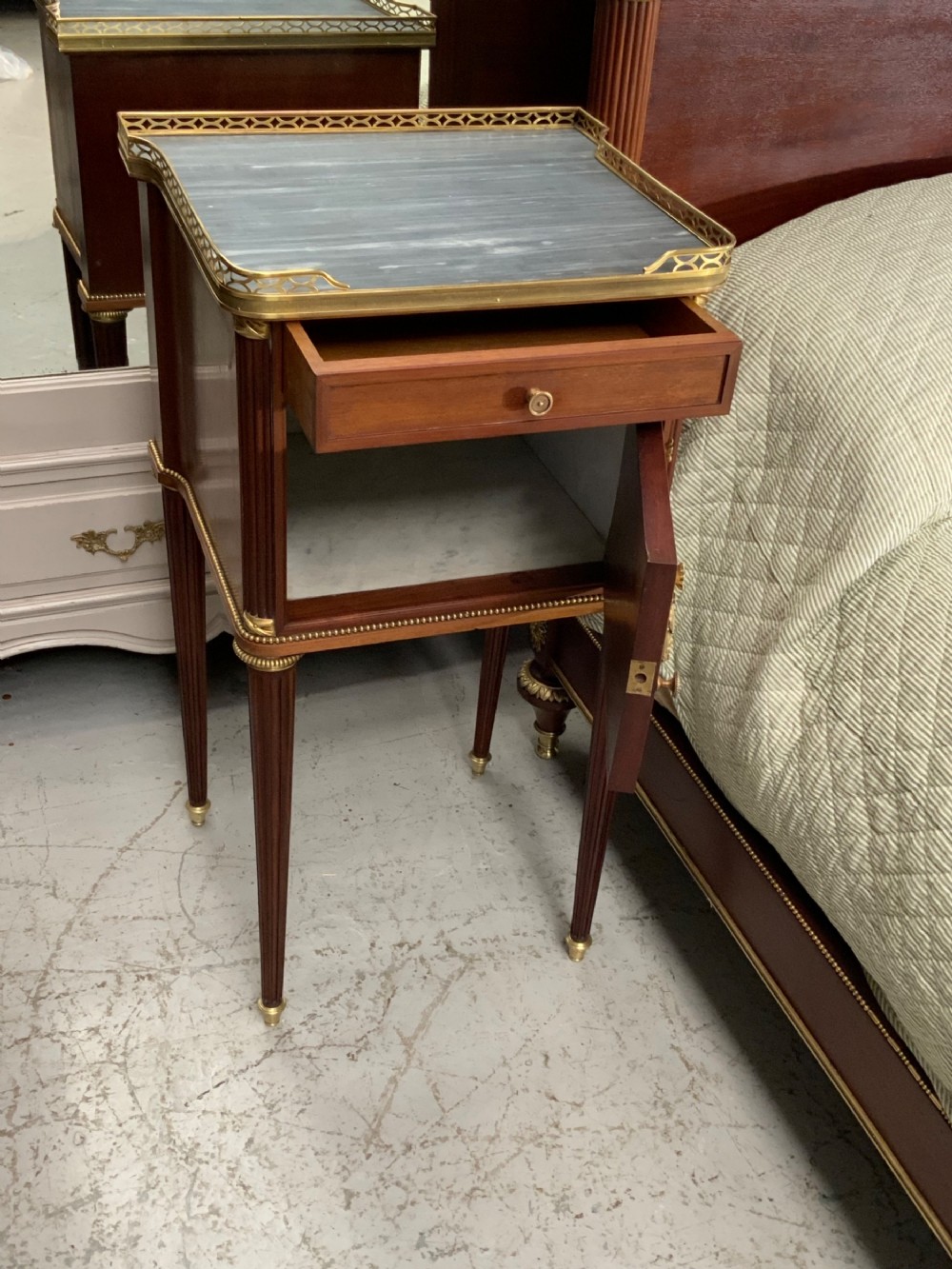French Neoclassical mahogany bed frame featuring an oval marquetry panel, polished brass mounts, fluted columns, and two matching marble-topped bedside cabinets. View XII