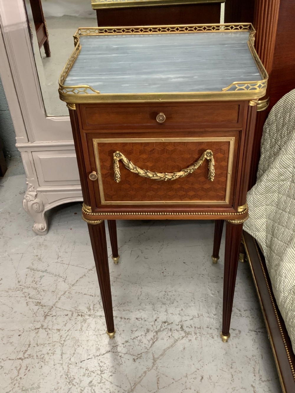 French Neoclassical mahogany bed frame featuring an oval marquetry panel, polished brass mounts, fluted columns, and two matching marble-topped bedside cabinets. View XIII