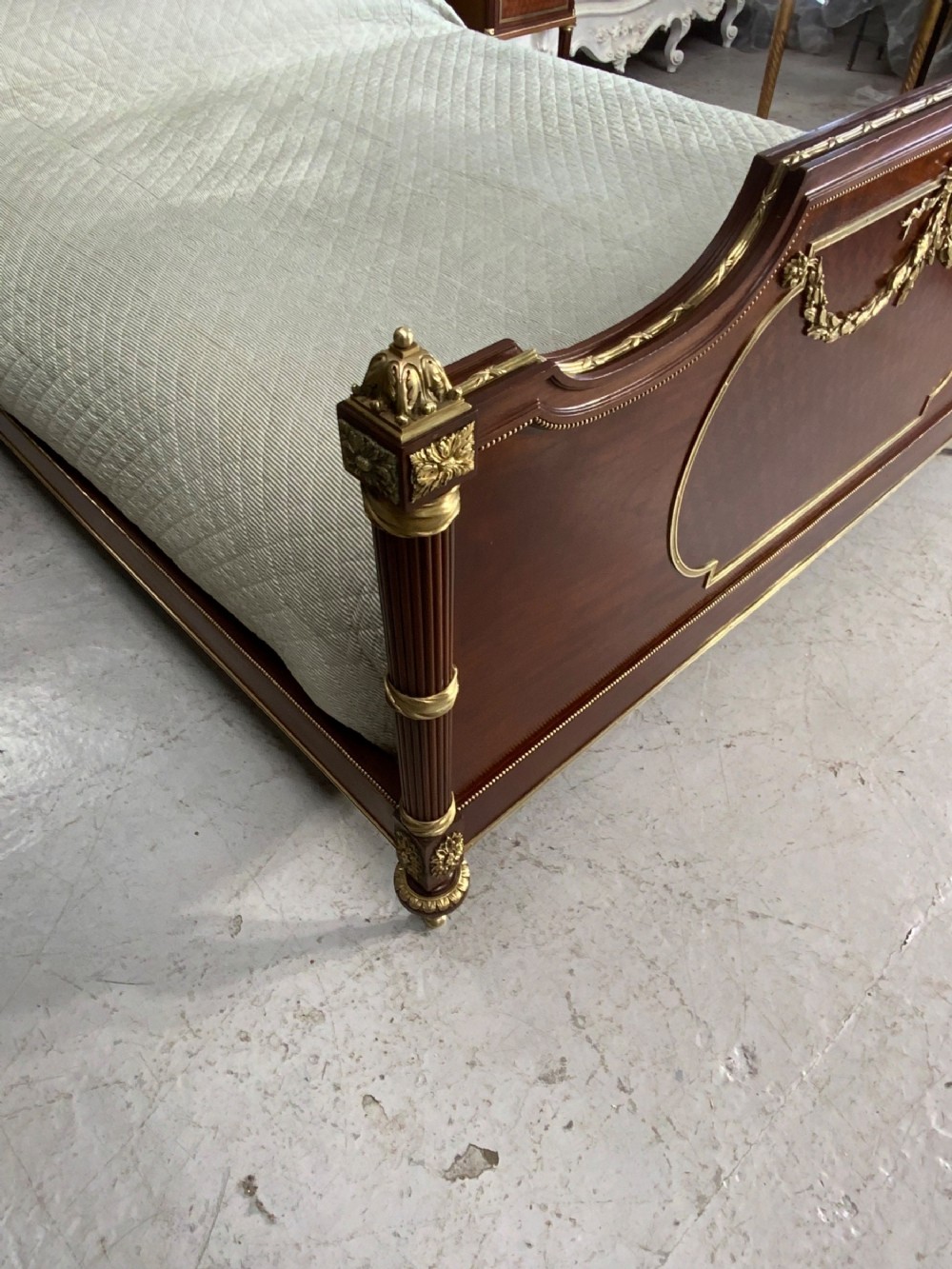 French Neoclassical mahogany bed frame featuring an oval marquetry panel, polished brass mounts, fluted columns, and two matching marble-topped bedside cabinets. View XVI