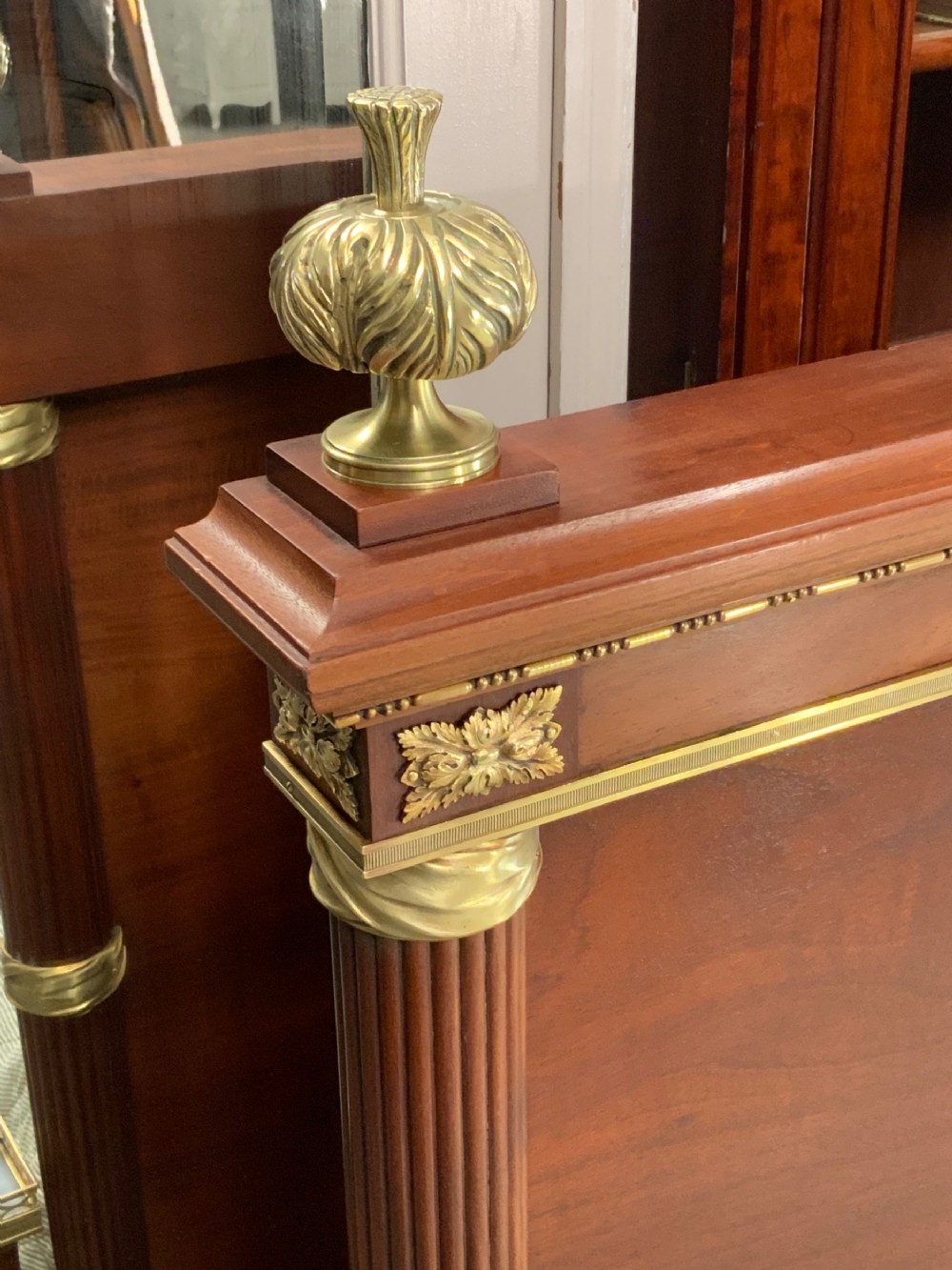 French Neoclassical mahogany bed frame featuring an oval marquetry panel, polished brass mounts, fluted columns, and two matching marble-topped bedside cabinets. View XVII