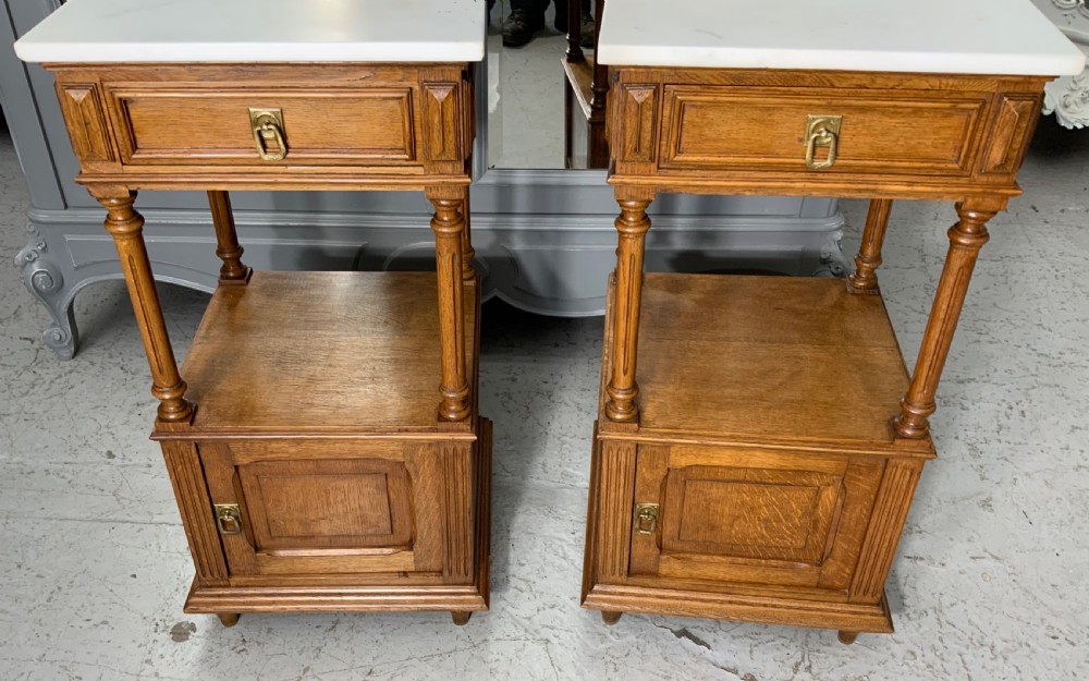 A pair of French oak bedside cabinets featuring white marble tops, single drawers, open shelf sections with turned columns, and lower cupboard doors. View III