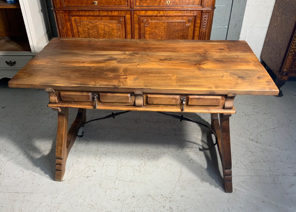 A solid walnut writing desk featuring two carved front drawers with iron drop handles, supported by splayed trestle legs and a curved wrought iron stretcher.