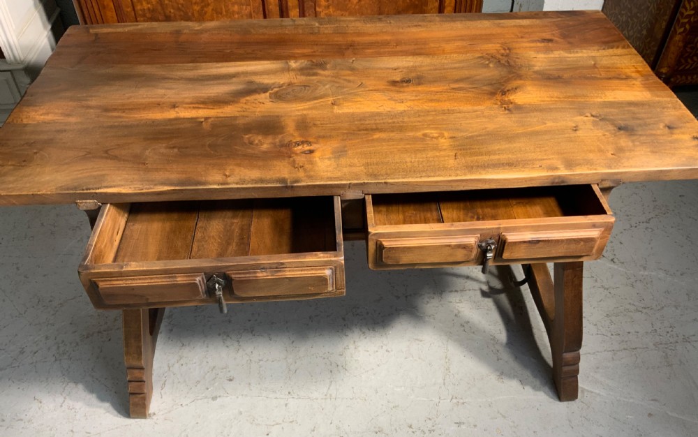 A solid walnut writing desk featuring two carved front drawers with iron drop handles, supported by splayed trestle legs and a curved wrought iron stretcher. View II