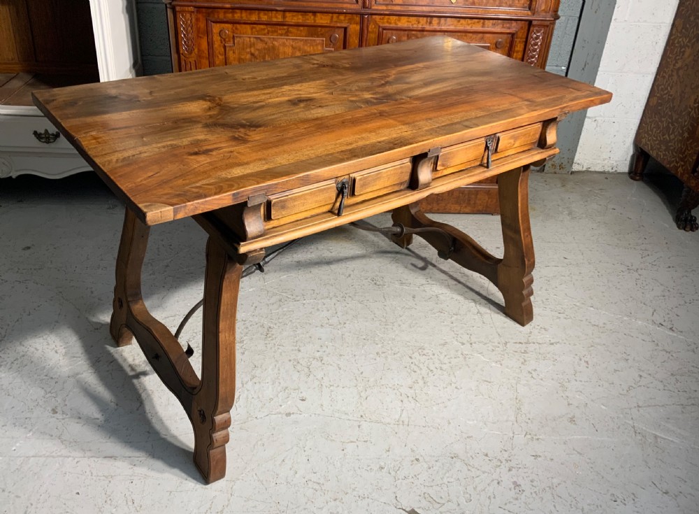 A solid walnut writing desk featuring two carved front drawers with iron drop handles, supported by splayed trestle legs and a curved wrought iron stretcher. View IV