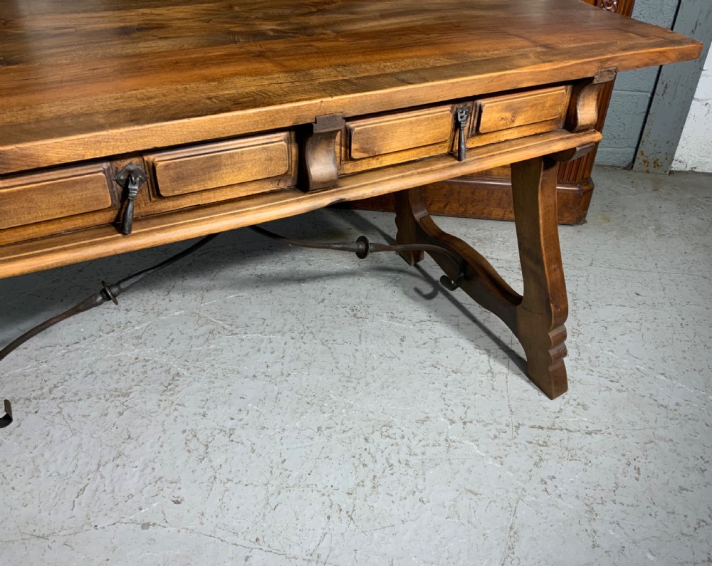 A solid walnut writing desk featuring two carved front drawers with iron drop handles, supported by splayed trestle legs and a curved wrought iron stretcher. View VII