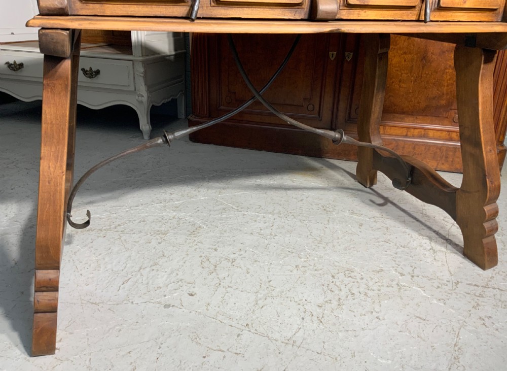 A solid walnut writing desk featuring two carved front drawers with iron drop handles, supported by splayed trestle legs and a curved wrought iron stretcher. View IX