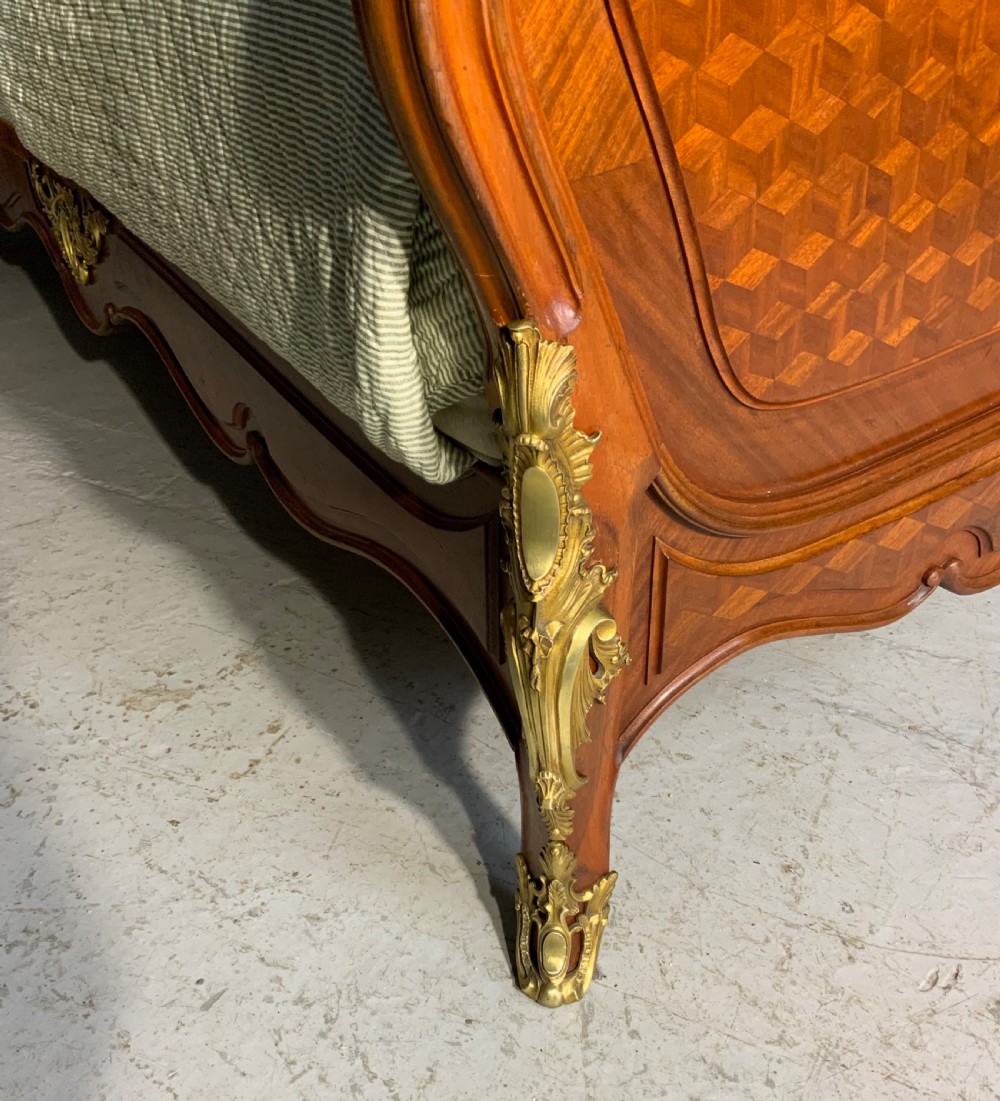 A French Louis XV style king-size bedstead featuring geometric parquetry inlay, carved central motif, and gilt-bronze mounts, flanked by two matching bedside cabinets with marble tops. View III