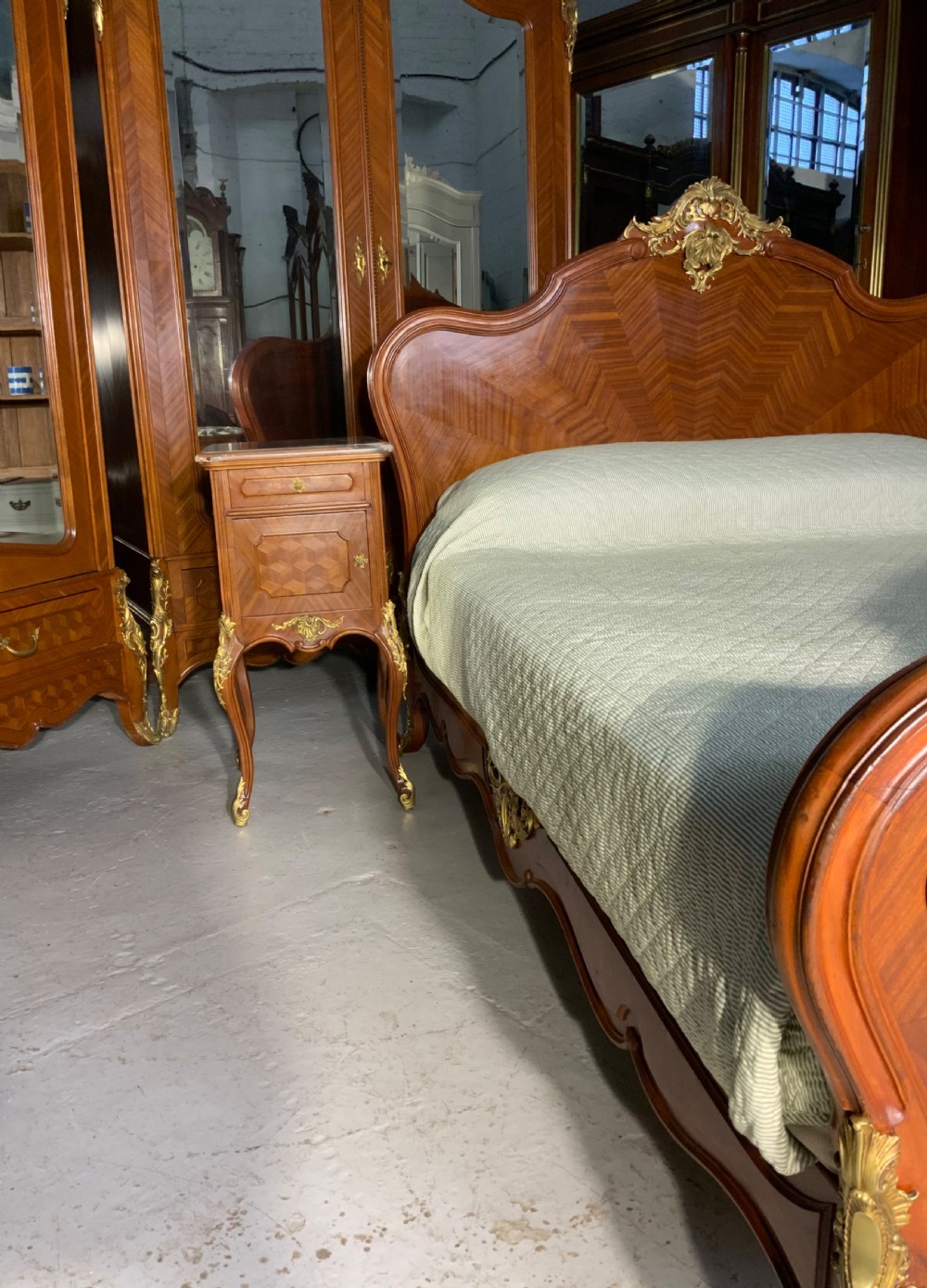 A French Louis XV style king-size bedstead featuring geometric parquetry inlay, carved central motif, and gilt-bronze mounts, flanked by two matching bedside cabinets with marble tops. View IV