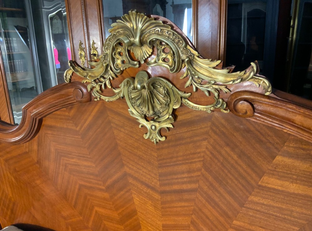 A French Louis XV style king-size bedstead featuring geometric parquetry inlay, carved central motif, and gilt-bronze mounts, flanked by two matching bedside cabinets with marble tops. View V