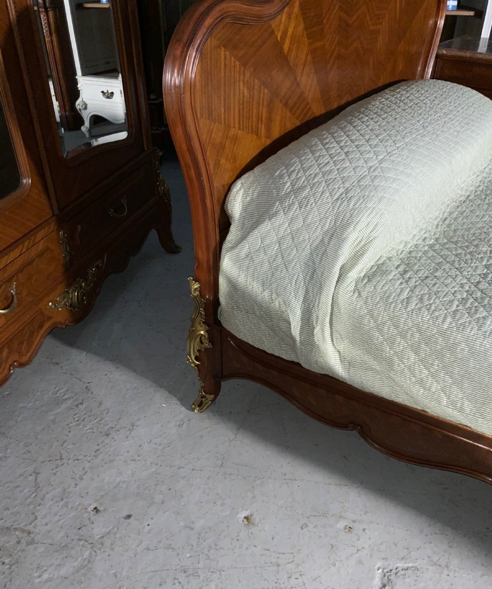 A French Louis XV style king-size bedstead featuring geometric parquetry inlay, carved central motif, and gilt-bronze mounts, flanked by two matching bedside cabinets with marble tops. View VII