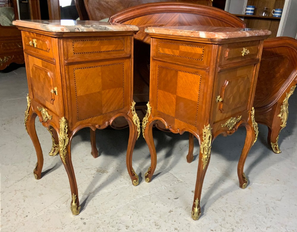 A French Louis XV style king-size bedstead featuring geometric parquetry inlay, carved central motif, and gilt-bronze mounts, flanked by two matching bedside cabinets with marble tops. View IX