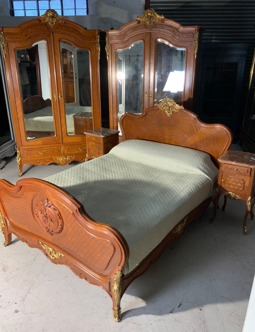 A French Louis XV style king-size bedstead featuring geometric parquetry inlay, carved central motif, and gilt-bronze mounts, flanked by two matching bedside cabinets with marble tops. View XIV