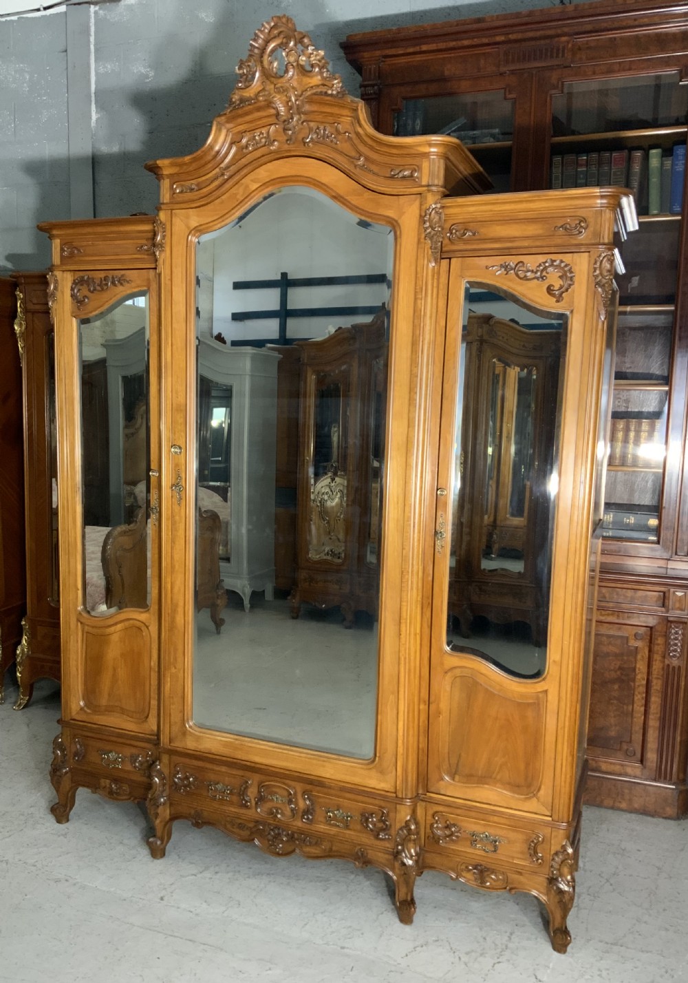 A large French carved walnut armoire featuring three mirrored doors, Rococo cresting pediment, and cabriole feet.