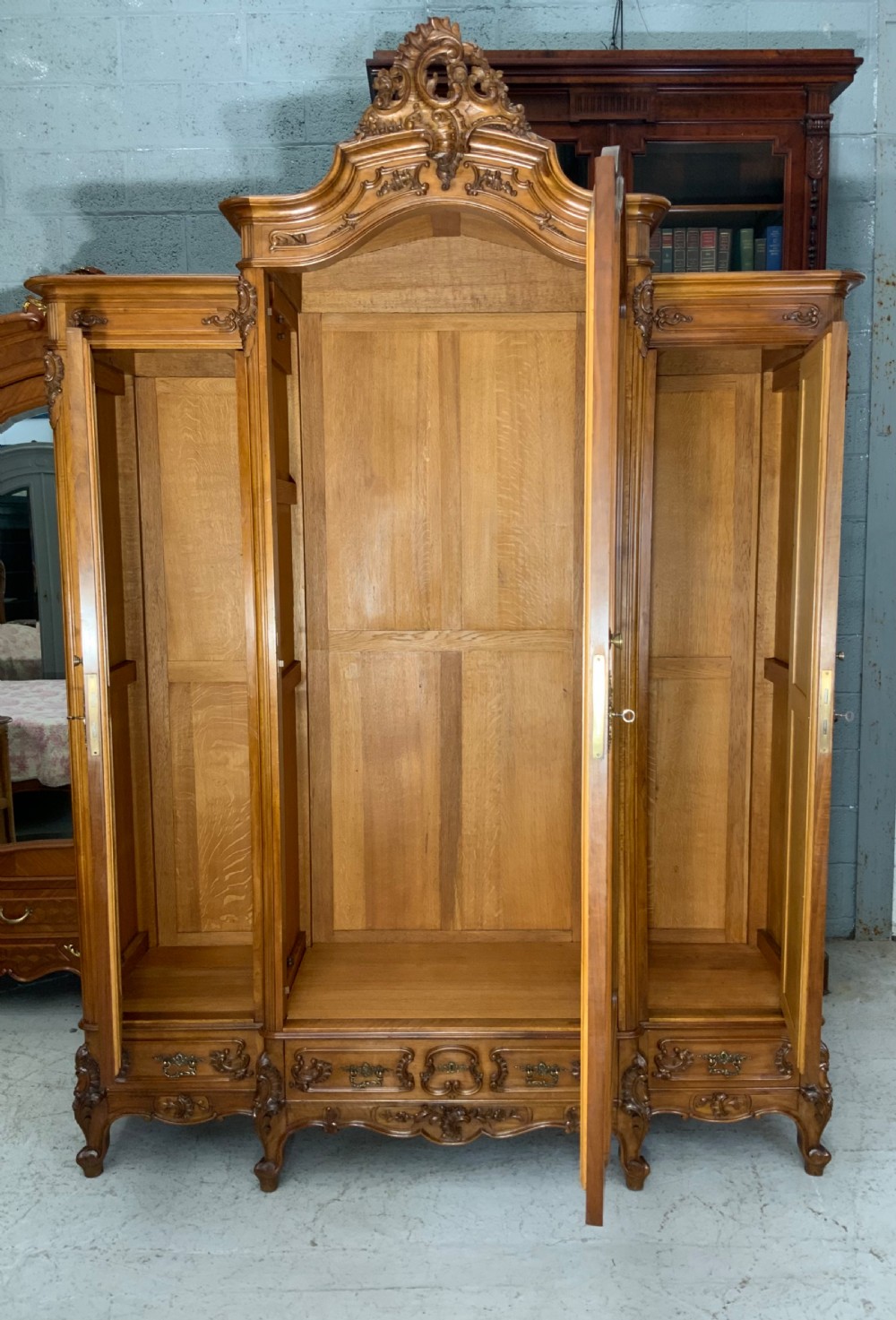 A large French carved walnut armoire featuring three mirrored doors, Rococo cresting pediment, and cabriole feet. View II