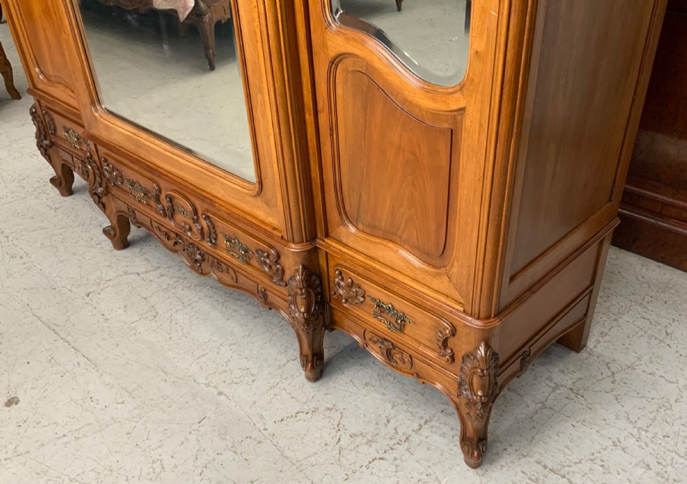 A large French carved walnut armoire featuring three mirrored doors, Rococo cresting pediment, and cabriole feet. View VIII