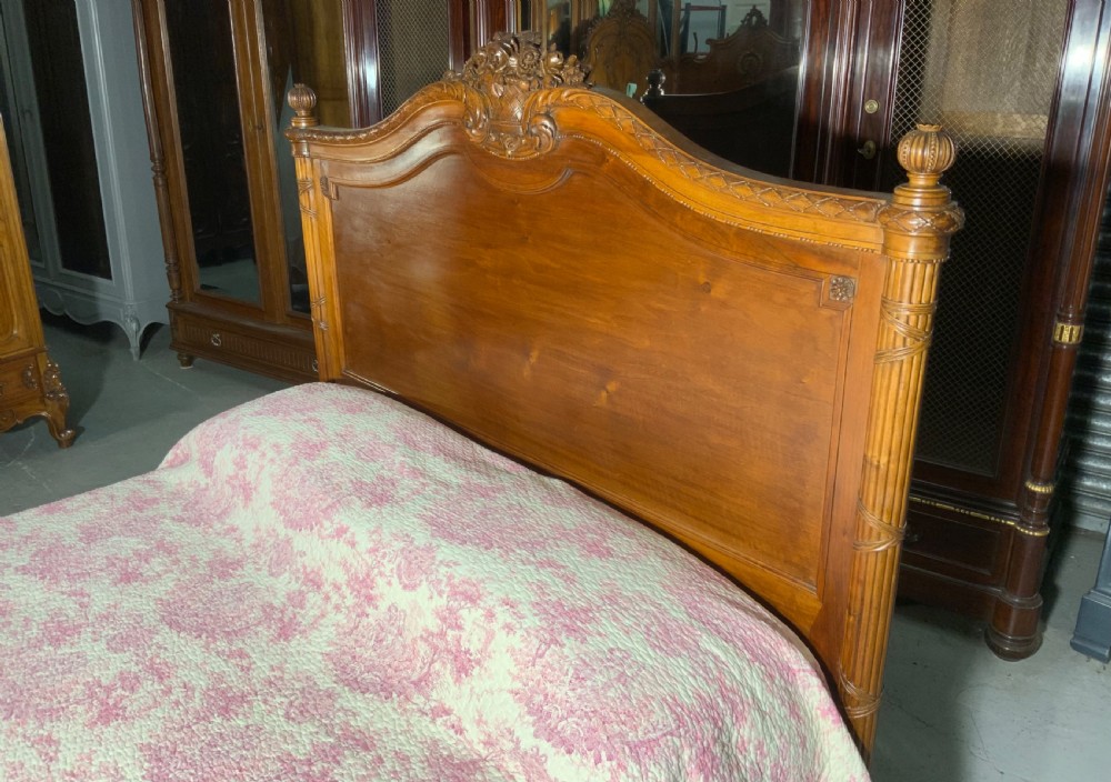 Carved mahogany king-size bedstead featuring fluted corner posts, an arched crest headboard, and carved leaf swags on the footboard. View X
