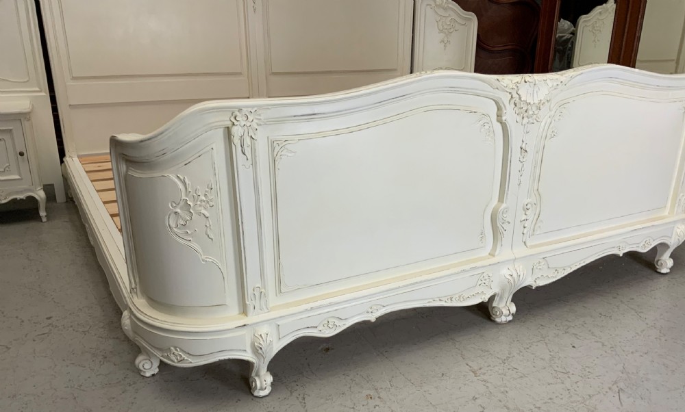 A cream painted French Rococo style bedstead featuring detailed foliage carving, serpentine headboard, matching footboard, and two bedside cabinets. View V