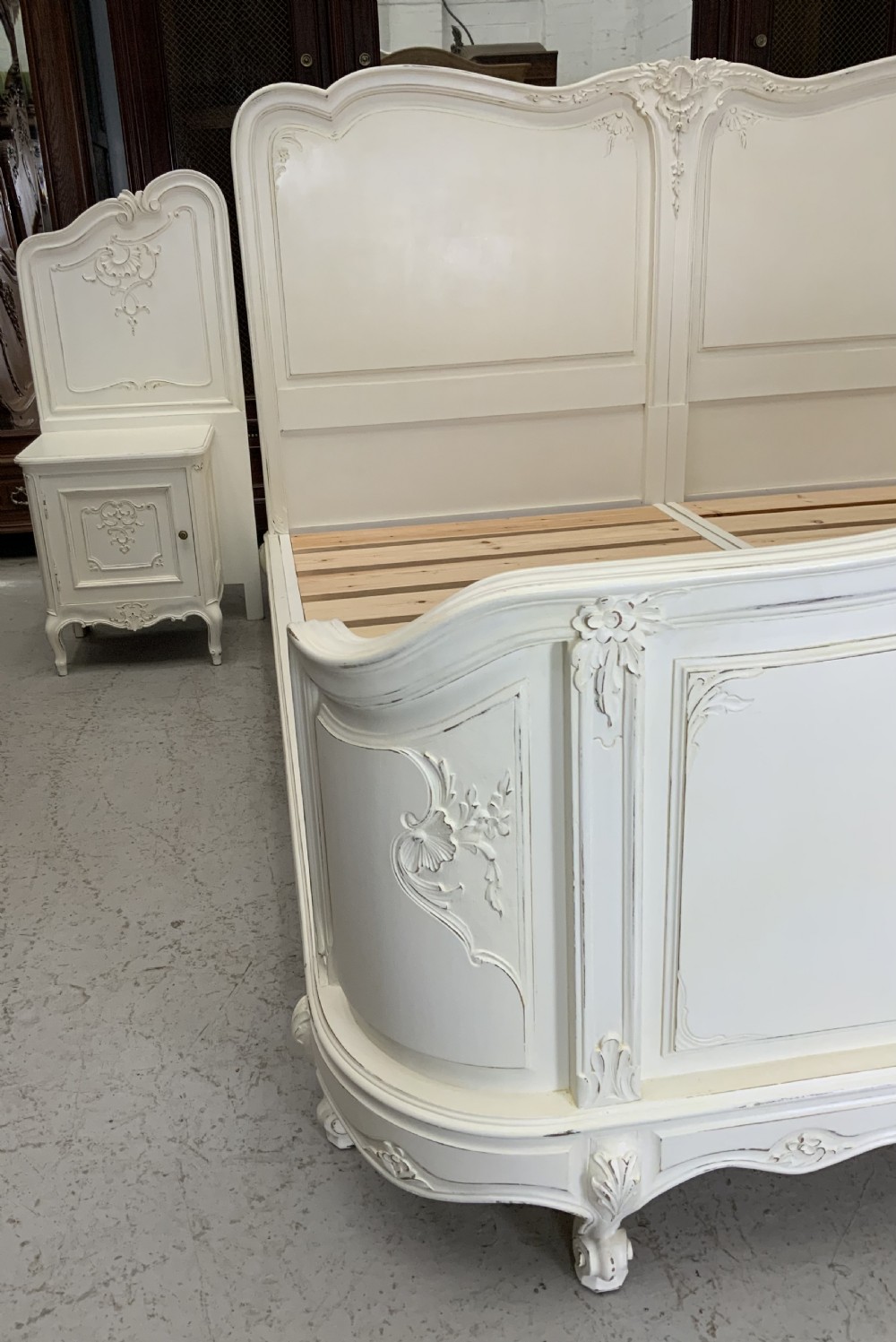 A cream painted French Rococo style bedstead featuring detailed foliage carving, serpentine headboard, matching footboard, and two bedside cabinets. View VII