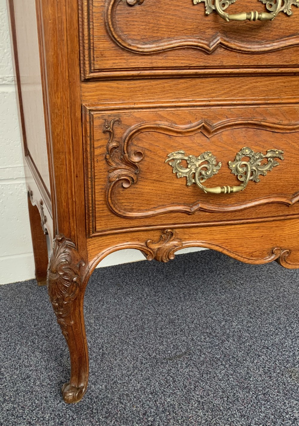 A carved oak French bow-front chest of drawers featuring two drawers with ornate brass handles, a shaped apron, and cabriole legs. View V