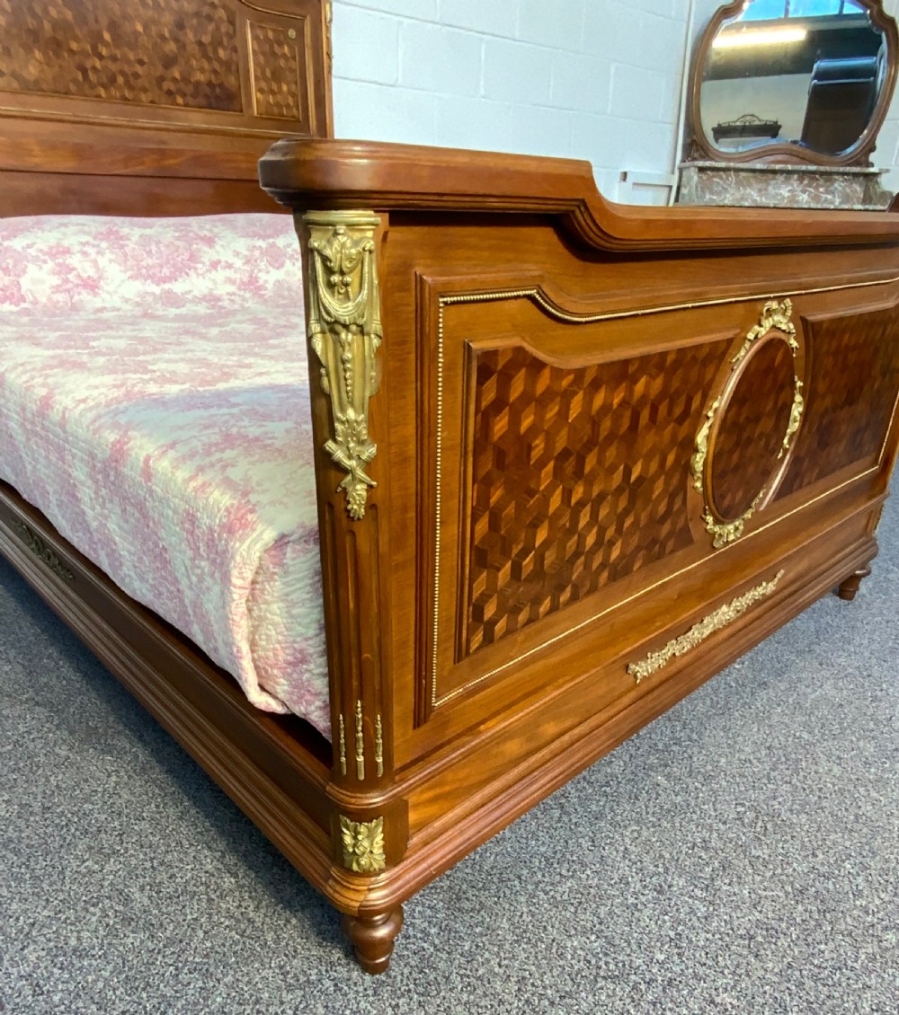 An antique French king-size wooden bed frame featuring detailed geometric parquetry inlay and decorative gilt bronze ormolu mounts on the headboard and footboard. View XIII