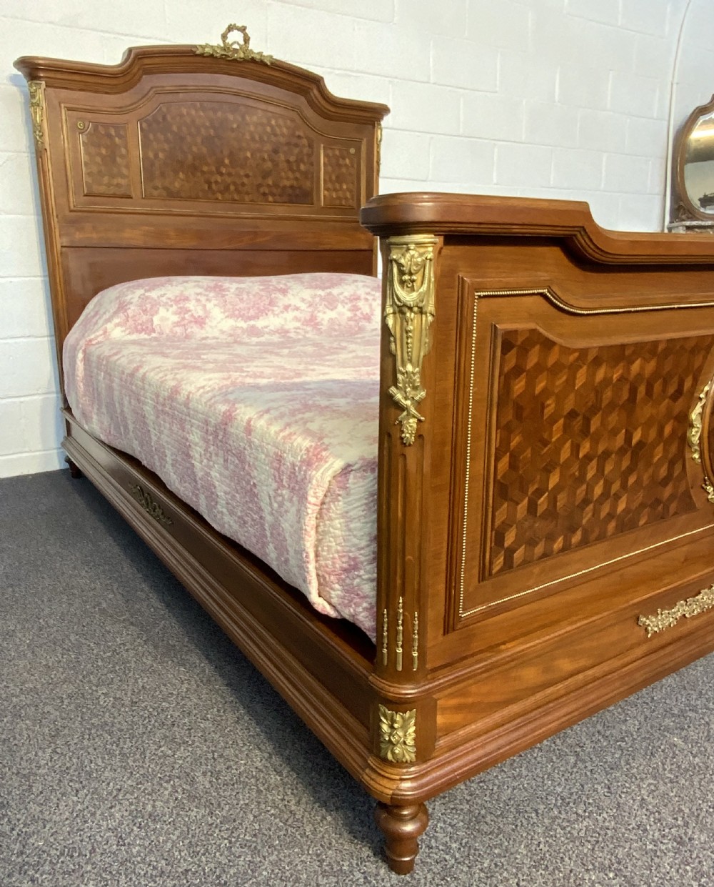 An antique French king-size wooden bed frame featuring detailed geometric parquetry inlay and decorative gilt bronze ormolu mounts on the headboard and footboard. View XIV