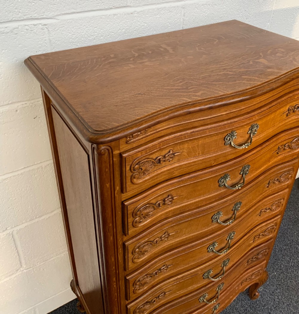 A tall French carved oak chest featuring seven drawers with brass handles, shell carvings, and cabriole feet. View II
