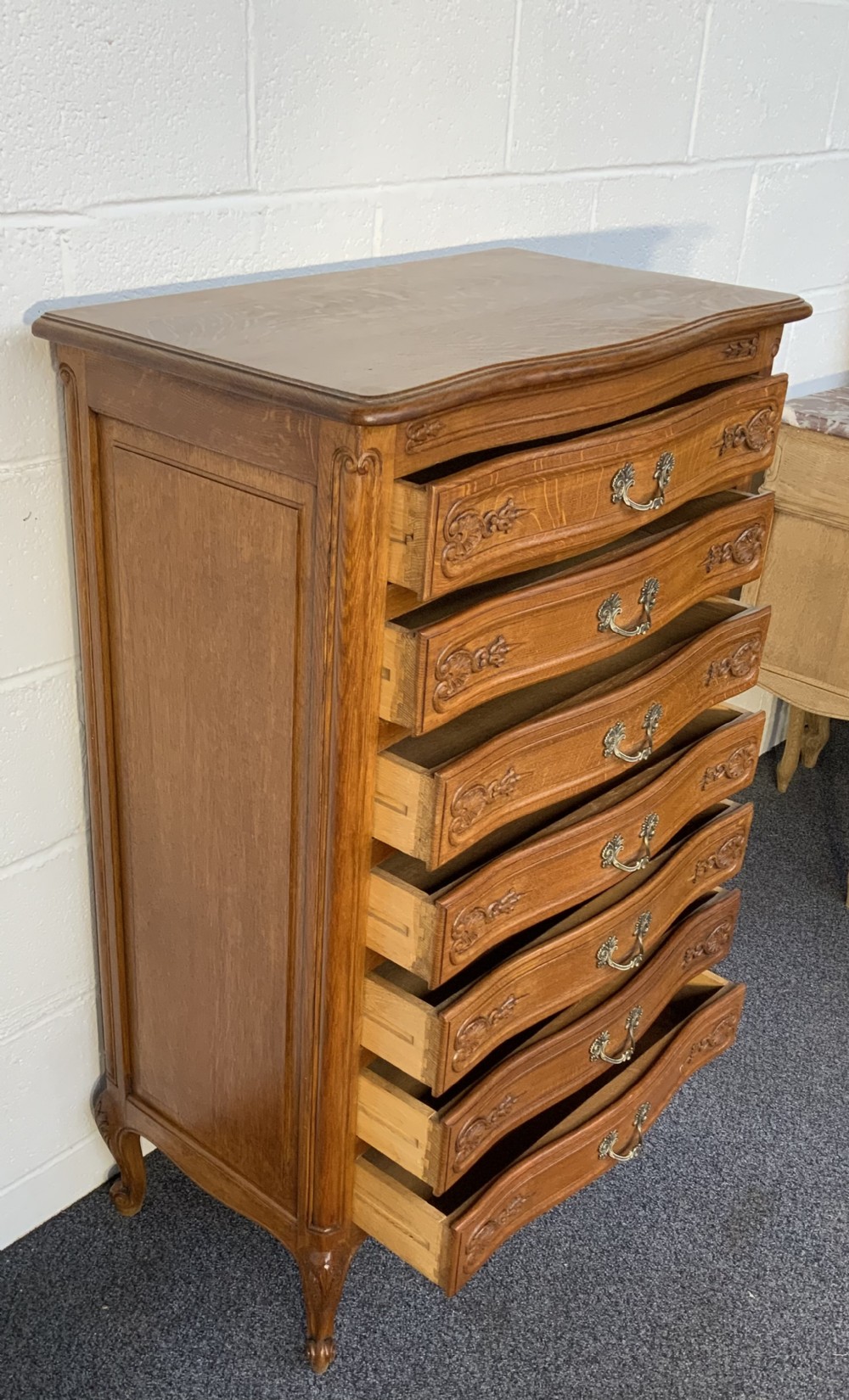 A tall French carved oak chest featuring seven drawers with brass handles, shell carvings, and cabriole feet. View VII
