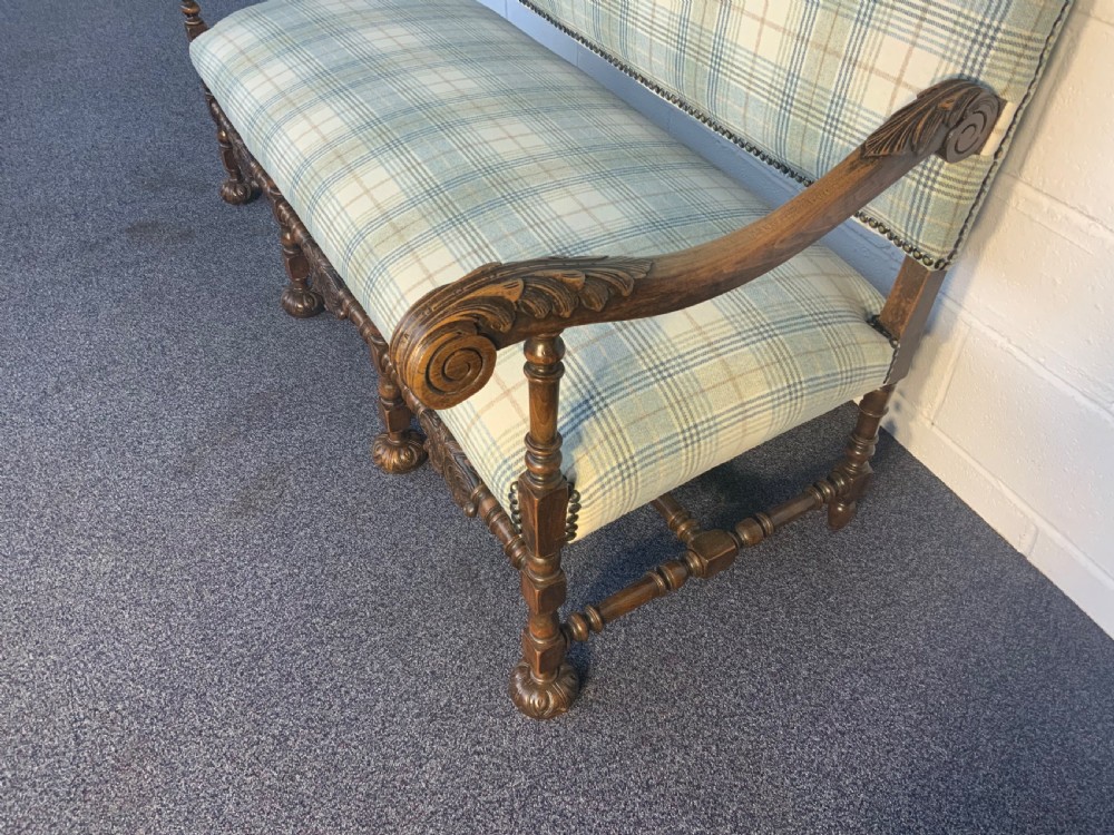 An upholstered French carved walnut settee featuring a green and cream check fabric, carved scroll arms, turned stretchers, and brass studding. View V