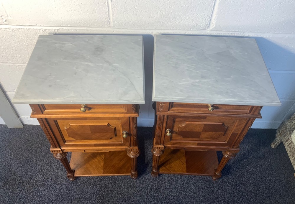 A pair of 19th-century French walnut bedside cabinets featuring grey marble tops, single drawers, cupboard doors with geometric panel mouldings, turned fluted legs, and lower open shelves. View VII
