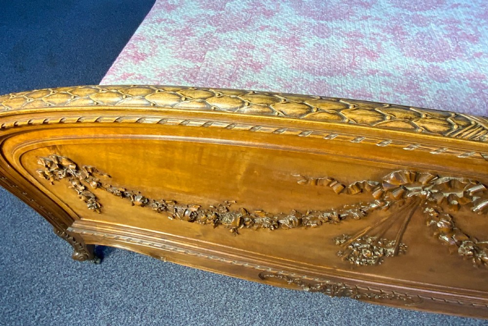 A carved walnut kingsize French bed frame featuring floral garland relief details on the curved footboard and an arched headboard. View VI