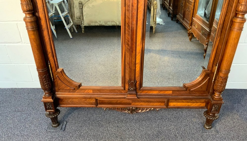 A tall 19th-century French rosewood armoire with two full-length mirrored doors, an arched pediment topped with a foliage crest carving, and fluted corner columns. View II