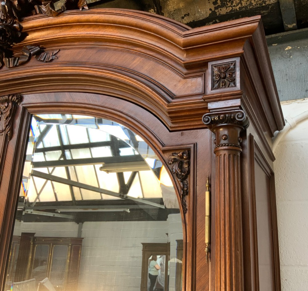 A tall 19th-century French rosewood armoire with two full-length mirrored doors, an arched pediment topped with a foliage crest carving, and fluted corner columns. View V