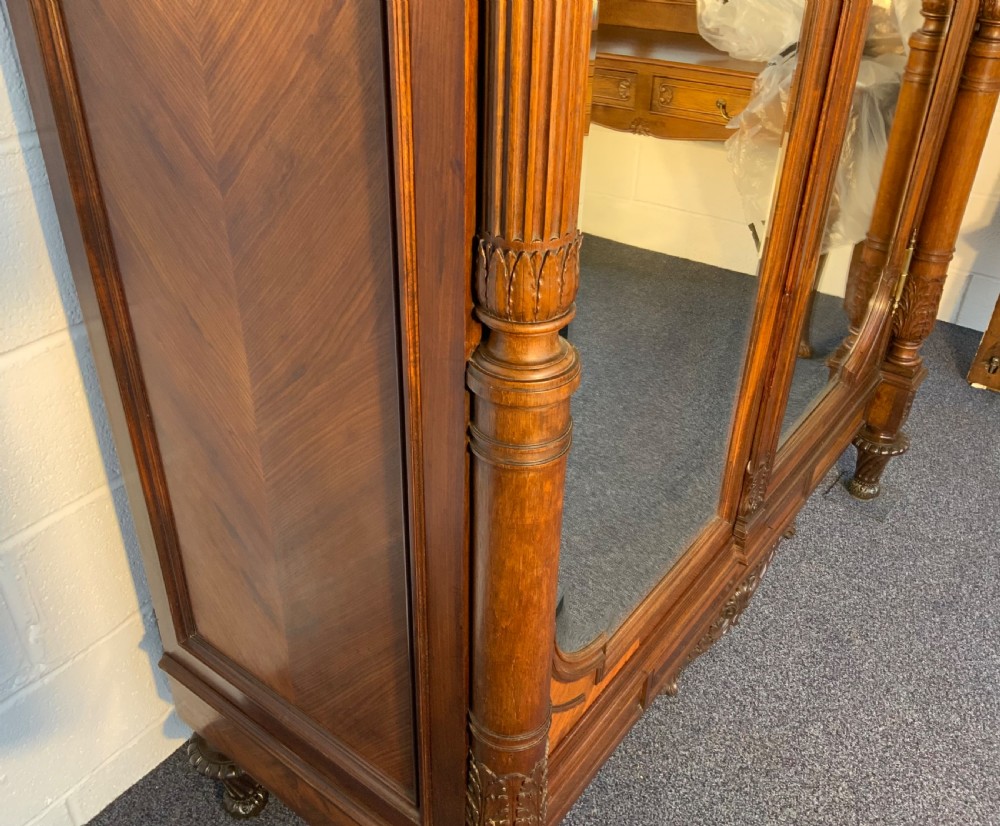 A tall 19th-century French rosewood armoire with two full-length mirrored doors, an arched pediment topped with a foliage crest carving, and fluted corner columns. View VII