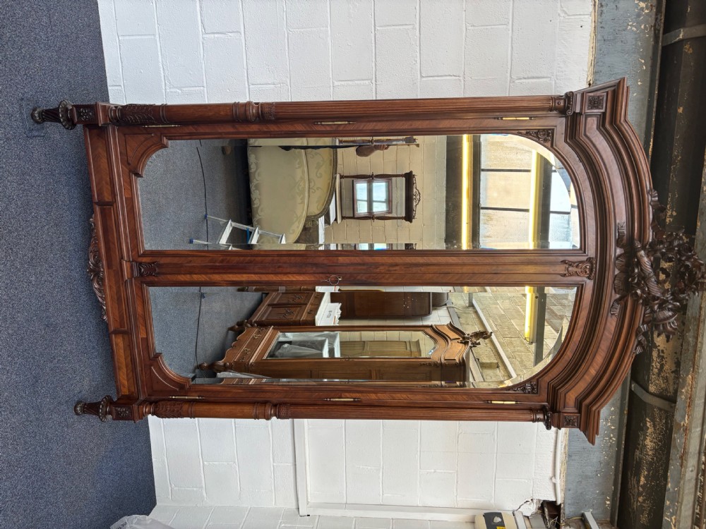 A tall 19th-century French rosewood armoire with two full-length mirrored doors, an arched pediment topped with a foliage crest carving, and fluted corner columns. View XV