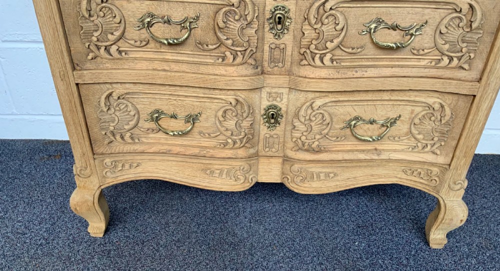 A light bleached oak French commode featuring three carved drawer fronts, brass handles, and short cabriole legs. View VII