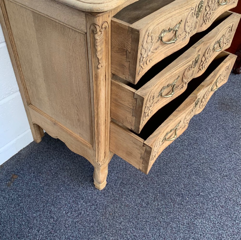 A light bleached oak French commode featuring three carved drawer fronts, brass handles, and short cabriole legs. View VIII