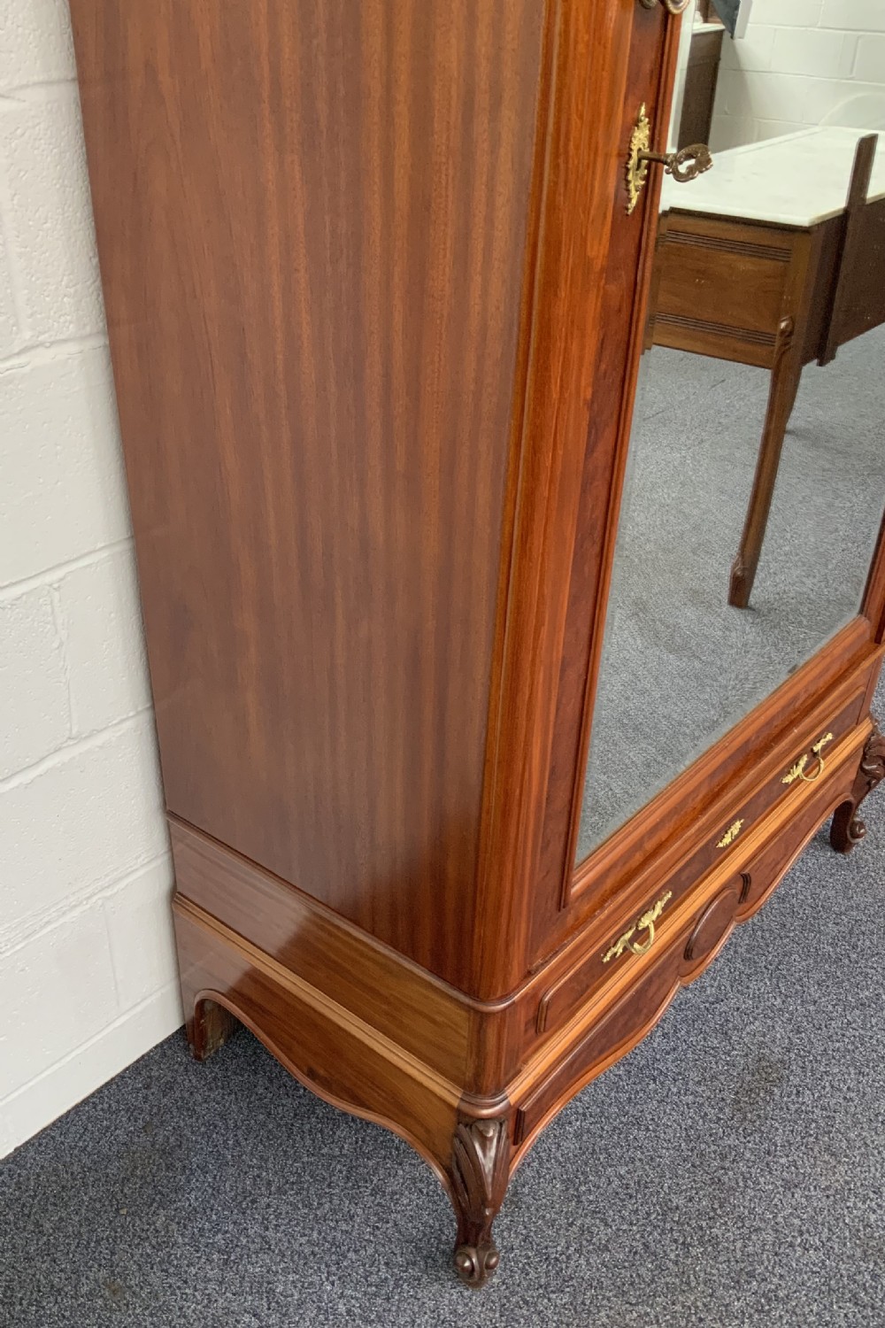 A tall single-door French mahogany armoire featuring an arched mirror door, detailed floral carved cresting, a bottom drawer, and cabriole feet. View VI