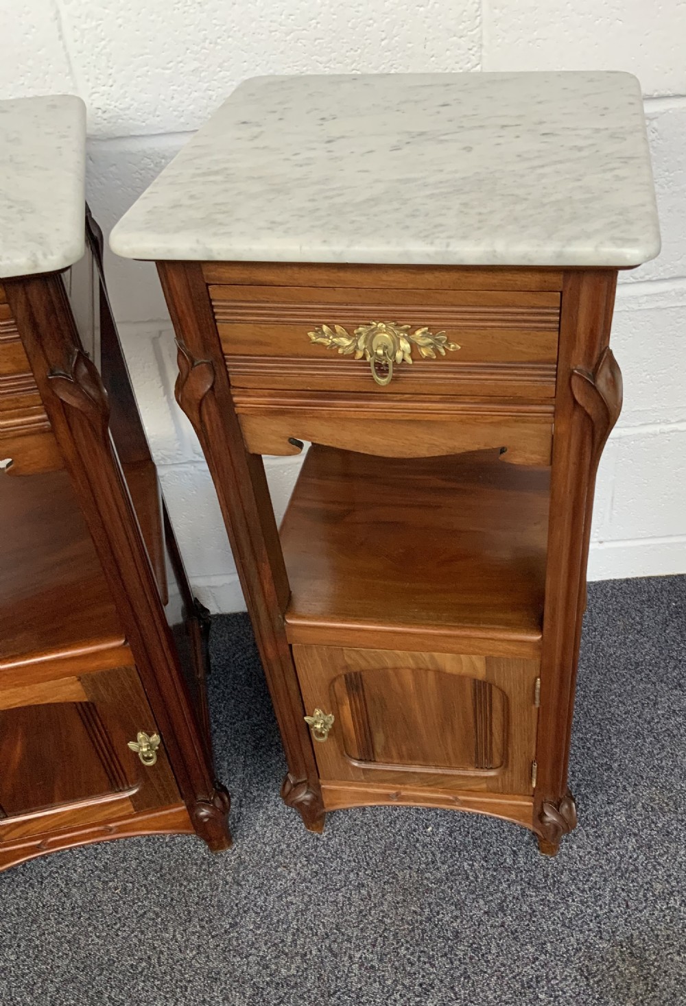 A pair of French Art Nouveau mahogany bedside cabinets featuring white marble tops, single drawers with brass handles, open middle shelves, and lower cupboards. View VI