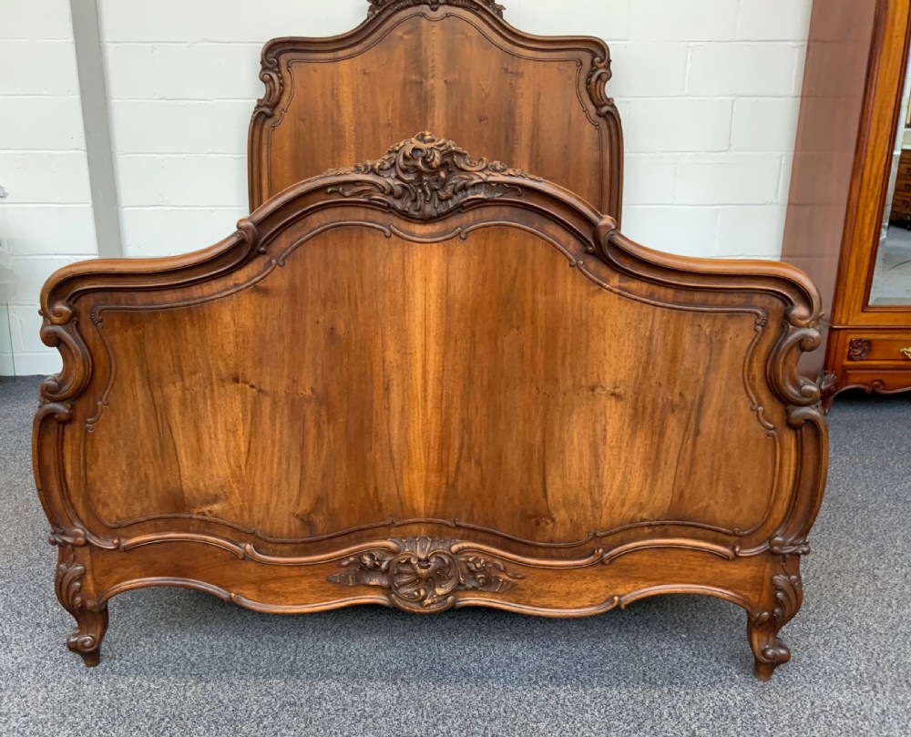 A carved walnut French bed frame featuring a high arched headboard and matching footboard decorated with rocaille crest carvings. View II